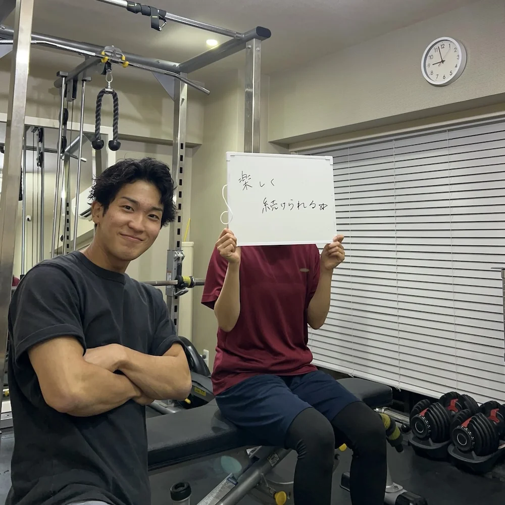 WORKOUTHOLIC田町・三田店で、トレーニング後に「楽しく続けられる♪」と書いたボードを持つ会員様とトレーナー