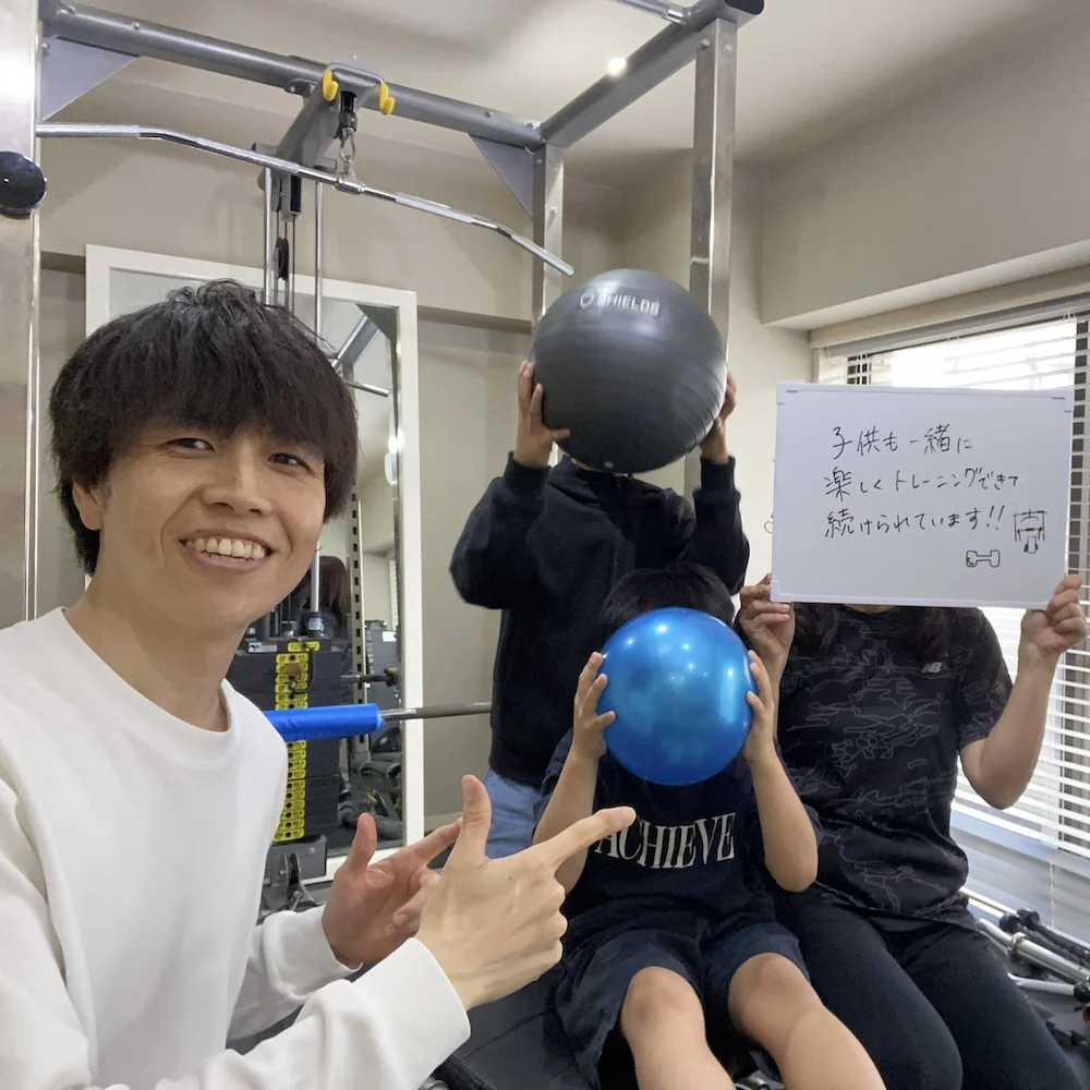 WORKOUTHOLIC田町・三田店で、トレーナーと一緒に子連れでトレーニングする30代女性会員とお子様2人の写真。「子供も一緒に楽しくトレーニングできて続けられています」と書かれたホワイトボードを掲げている
